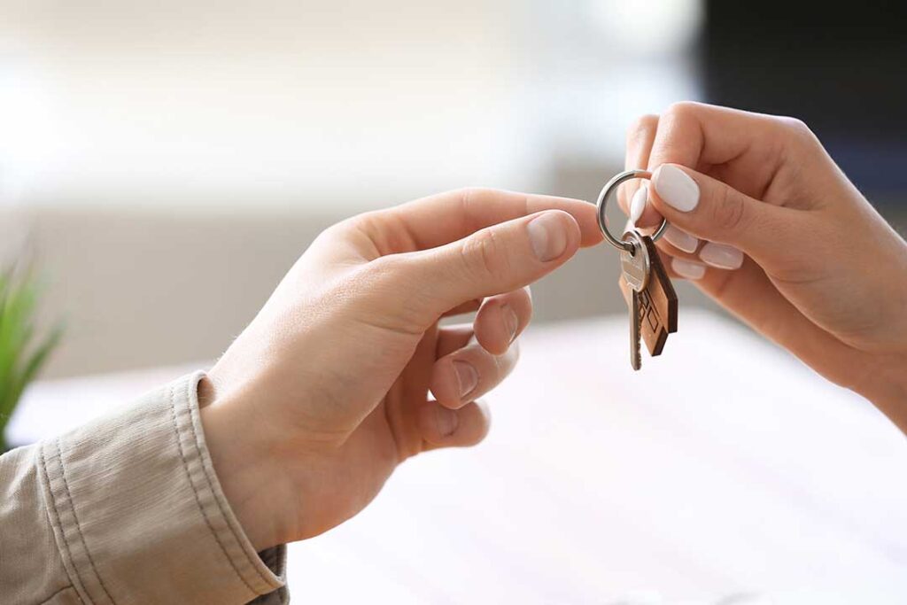 A person holding a clipboard and speaking with a homeowner in a living room during a real estate consultation.