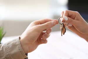 A person holding a clipboard and speaking with a homeowner in a living room during a real estate consultation.